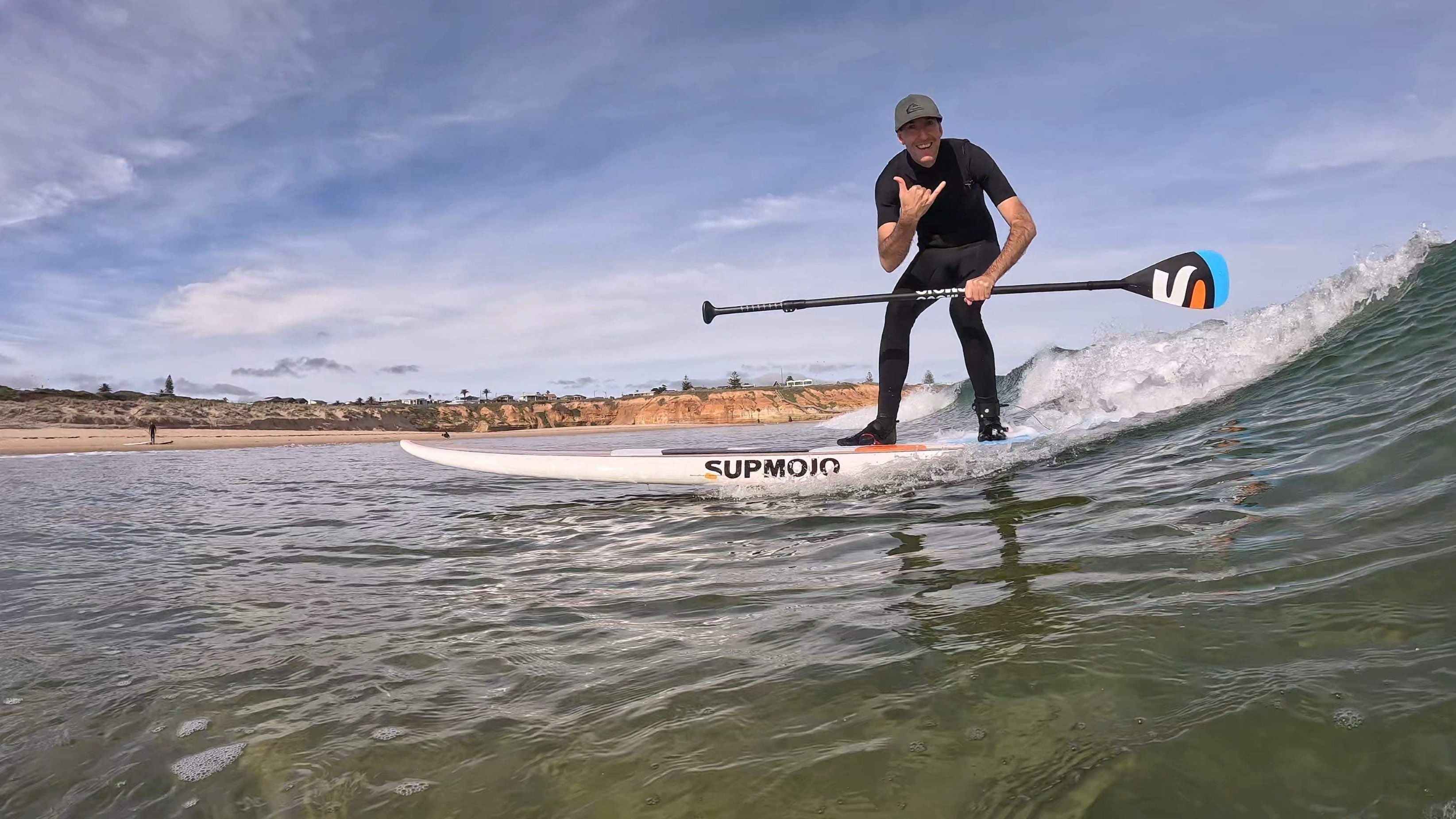 Person paddleboarding on a wave with a clear sky and beach in the background